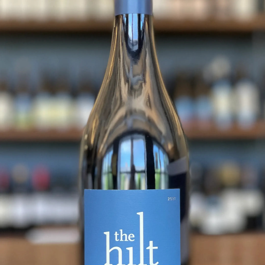 Wine bottle with blue label titled 'the hilt' against a blurred bar background