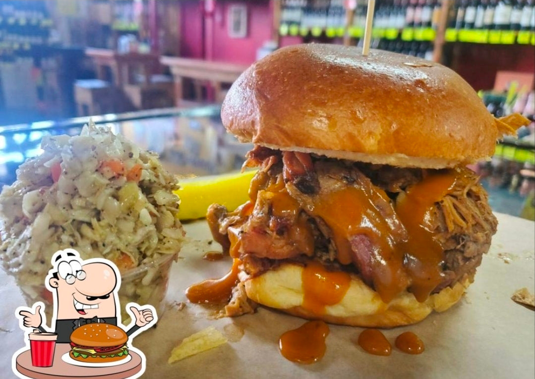 Large burger with cheese and sauce on a bun, next to coleslaw and a pickle, in a casual dining setting.